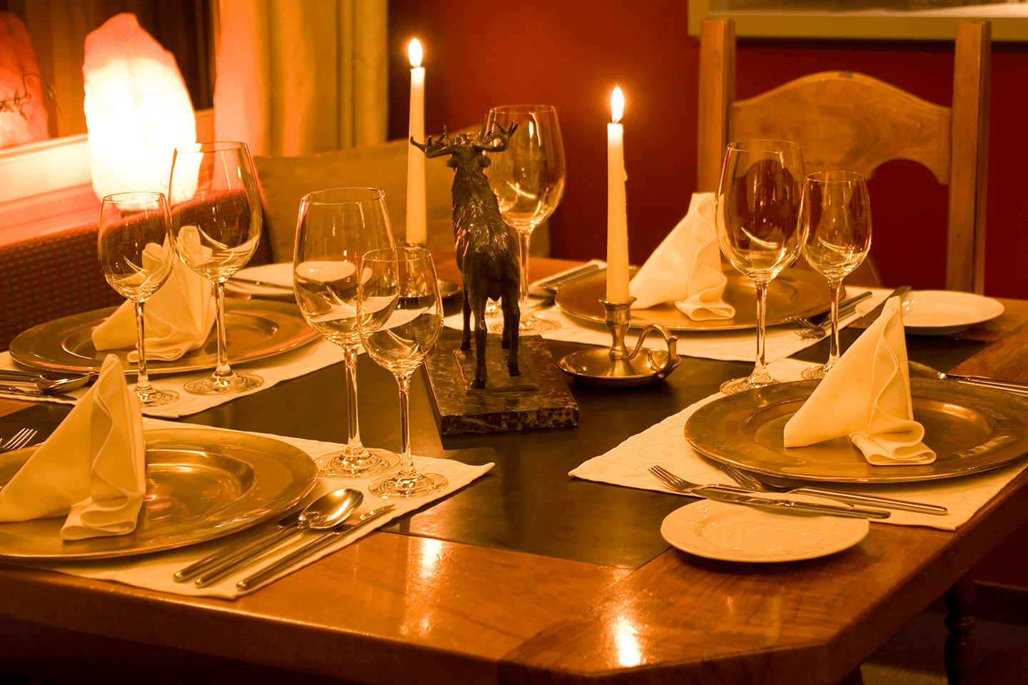 Candle lit dining table fully set with meal service for 4, including well folded napkins atop the plates.